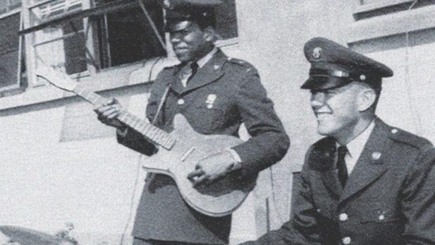 Black and white photograph of Jimi Hendrix and another soldier from the 101st Airborne playing guitars together at Fort Campbell, Kentucky. Both men are dressed in military uniforms, with Hendrix deeply engrossed in his performance.