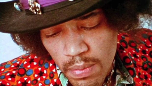 Jimi Hendrix wearing his iconic hat while passionately playing a blues riff on his guitar.