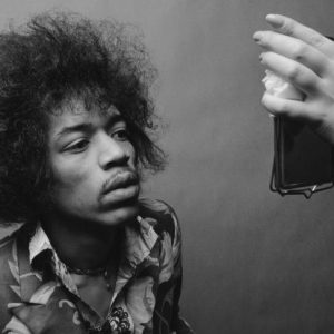 Jimi Hendrix, with his signature afro and vibrant attire, gazing intently into a mirror.