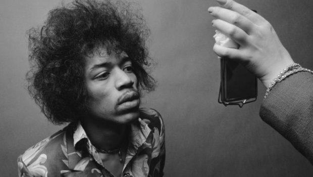 Jimi Hendrix, with his signature afro and vibrant attire, gazing intently into a mirror.