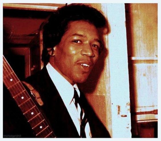 A photograph of a young Jimi Hendrix from 1964, during his pre-fame years on the Chitlin' Circuit, holding his guitar.