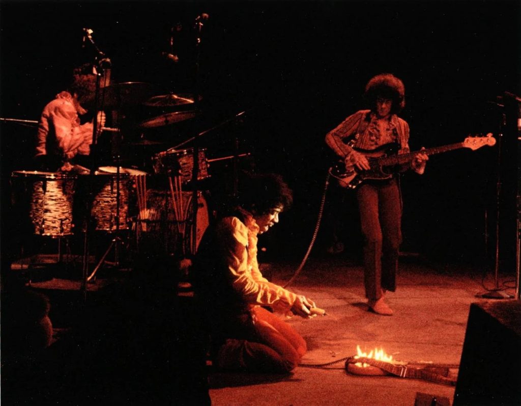 Jimi Hendrix kneeling on stage, setting his guitar on fire during his performance at the Monterey Pop Festival.