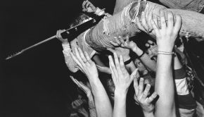 Kurt Cobain crowdsurfing with a guitar on top of an enthusiastic audience.