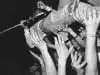 Kurt Cobain crowdsurfing with a guitar on top of an enthusiastic audience.