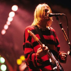 Kurt Cobain wallpaper performing on stage, dressed in his iconic red and black grunge outfit.