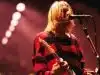 Kurt Cobain wallpaper performing on stage, dressed in his iconic red and black grunge outfit.