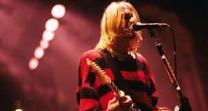 Kurt Cobain wallpaper performing on stage, dressed in his iconic red and black grunge outfit.